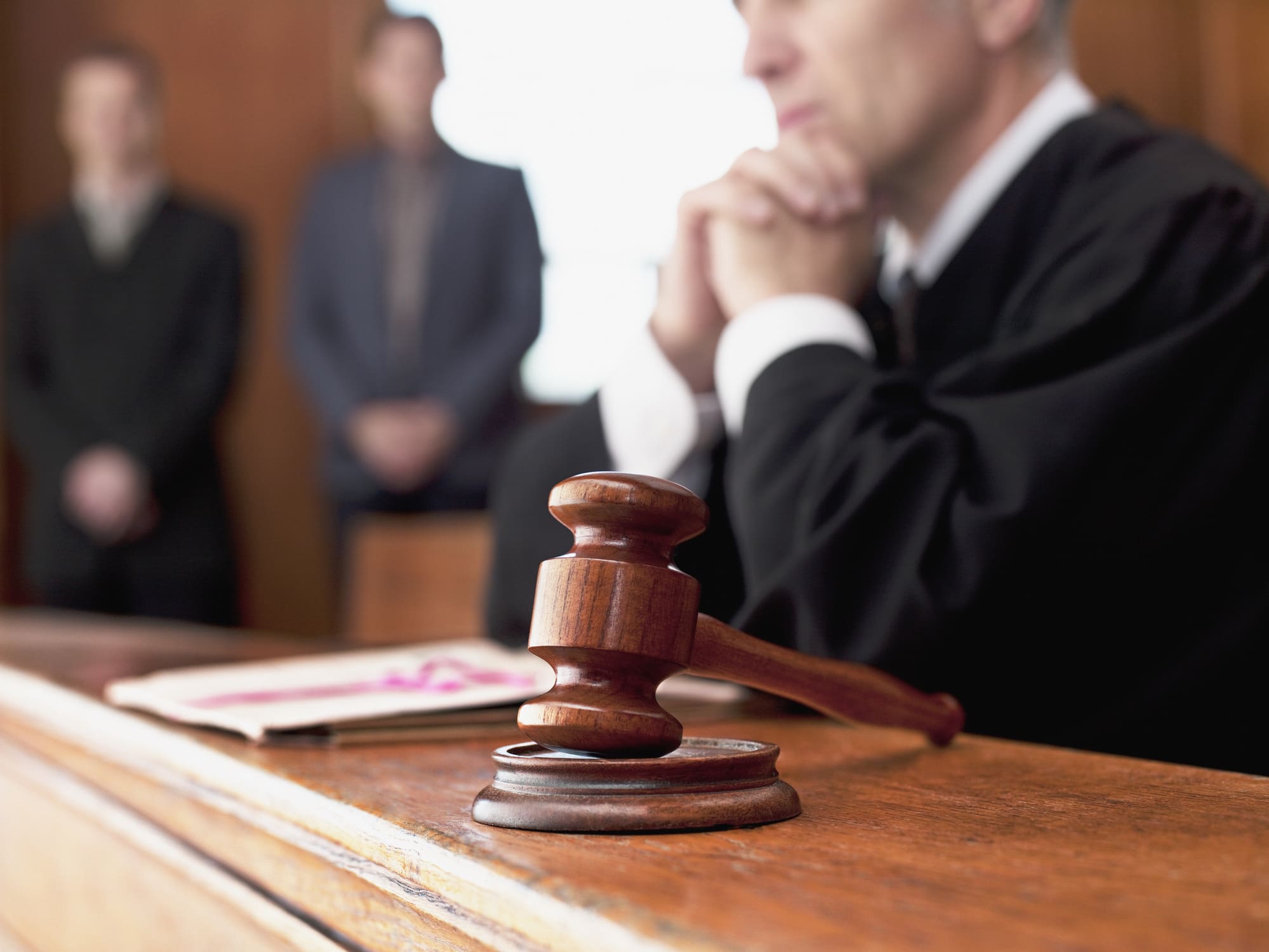 Close-up of a judge’s gavel in a courtroom with people standing before the bench, illustrating traditional court divorce proceedings